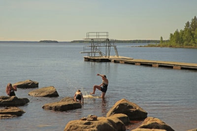 Kuvassa on järvimaisema, uimareita ja laituri.
